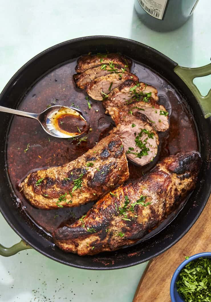 Sliced pork tenderloin in the oven on a board with pan sauce