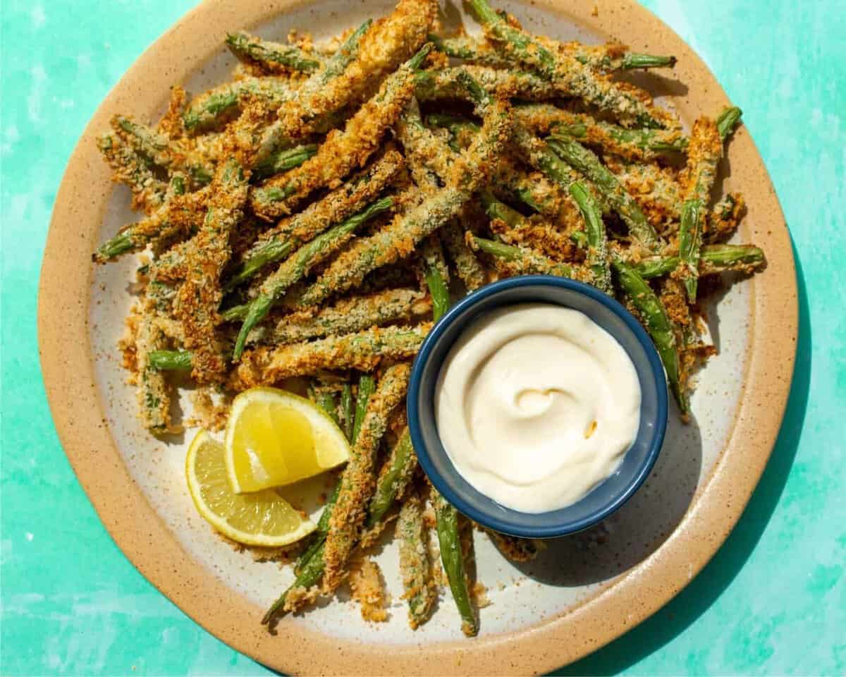 Golden browned green beans on a palte with some mayonaise in a small blue bowl.