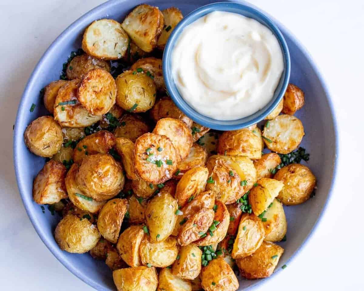 Air Fryer new potatoes in a blue bowl garnished with chives and served with dipping sauce.