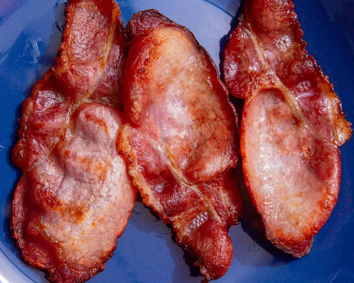 3 rashers of cooked, browned lean bacon on a blue plate.