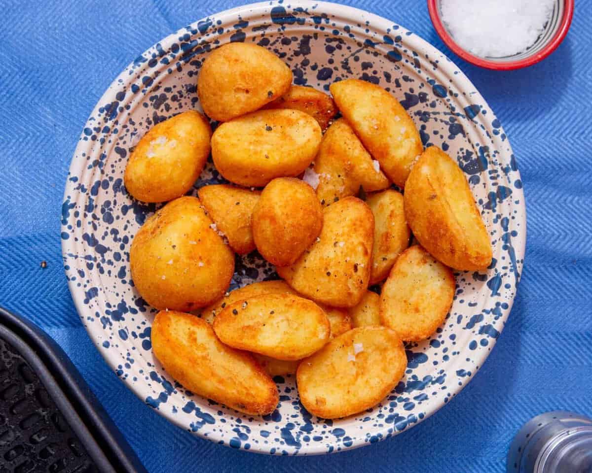 Golden browned roast potatoes in a patterned white and blue bowl on a blue background.