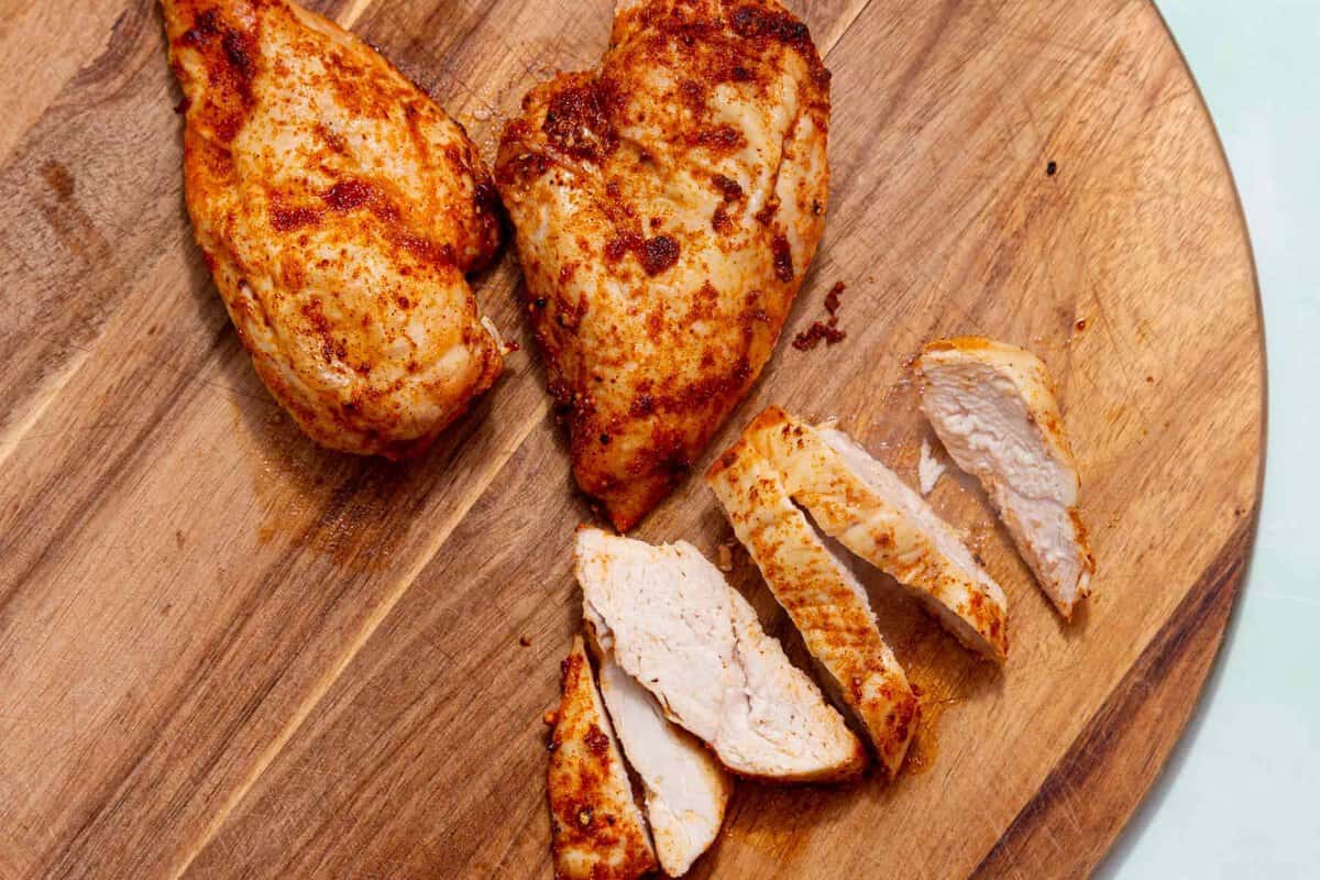 Golden browned, seasoned chicken breast fillets on a wooden board with one piece sliced.
