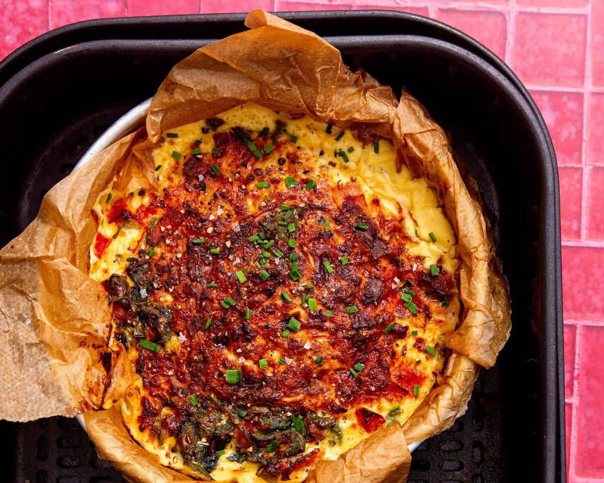 fully cooked air fryer frittata in an air fryer on a pink and white background