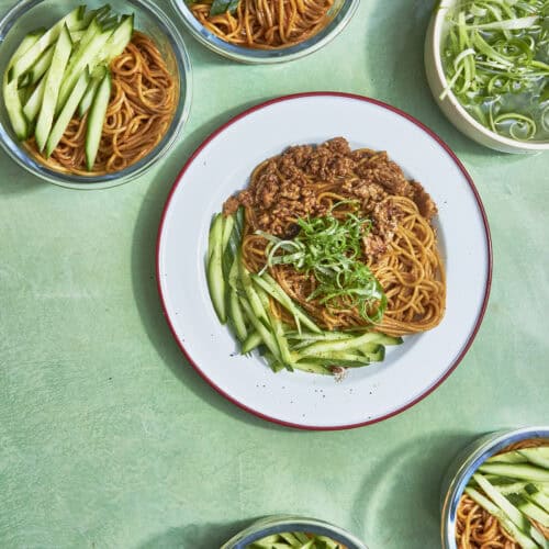 Chicken hoisin noodles divided into meal prep containers with curled spring onions