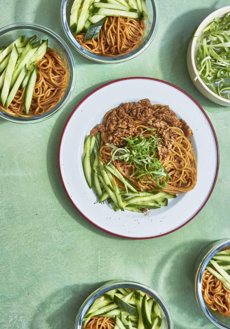 Chicken hoisin noodles divided into meal prep containers with curled spring onions