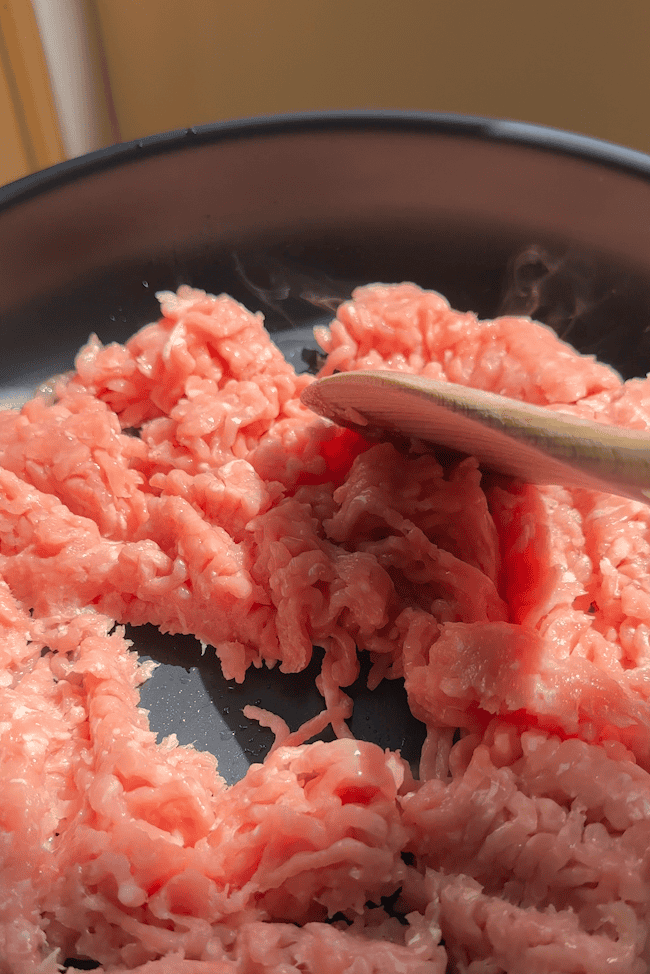 Chicken mince browning in a frying pan with olive oil, salt and pepper