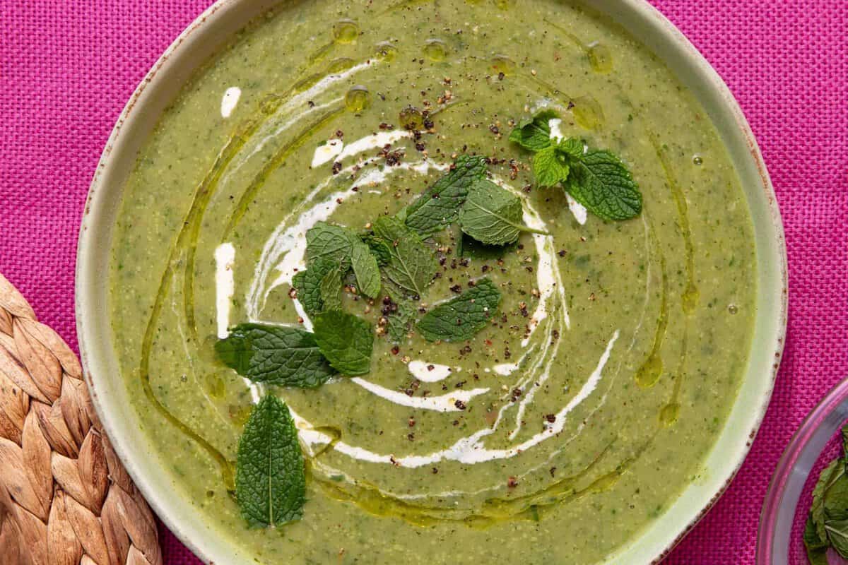 A bowl of courgette soup with a swirl of cream and fresh mint.
