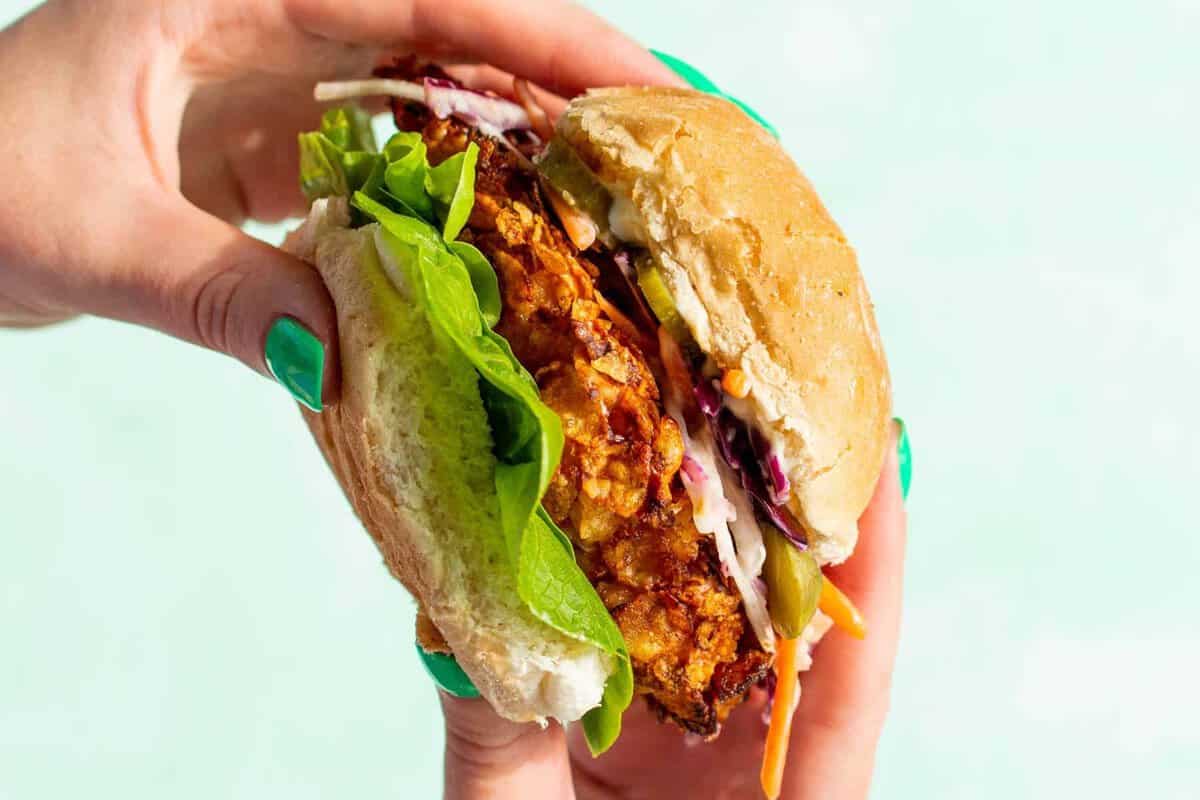 Spicy chicken sandwich side shot with hands holding the bun filled with lettuce, large piece of chicken and coleslaw.