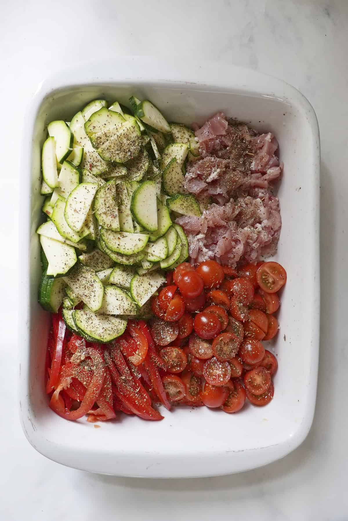 Cherry tomatoes, courgette, bacon and red pepper in a large baking tray with olive oil and herbs