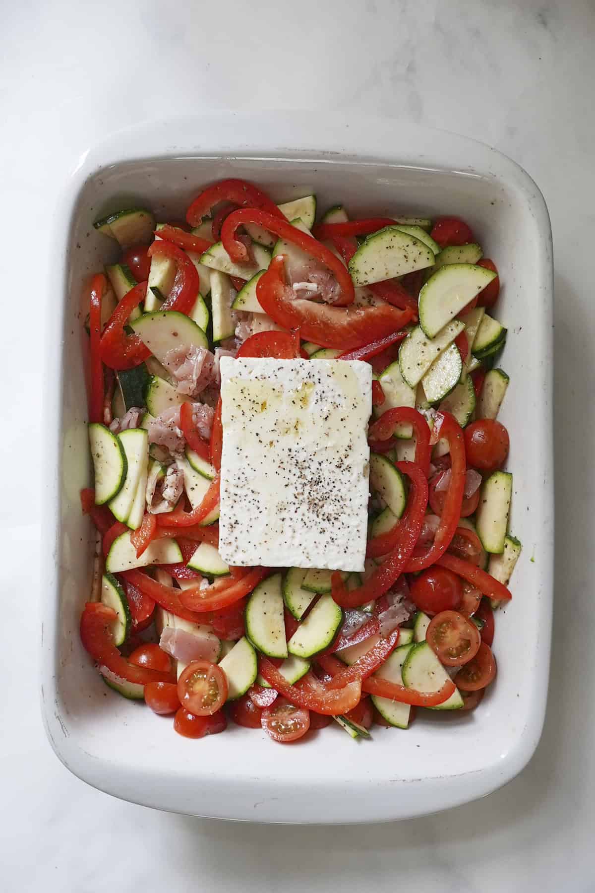 Block of feta placed on top of the veg and bacon tray before going in the oven
