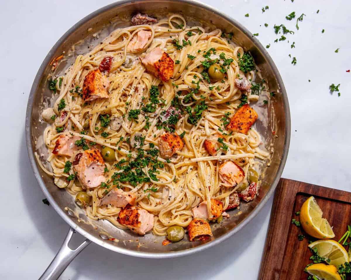 fully made salmon pasta dish in a skillet topped with fresh parsley and all on a grey-white background