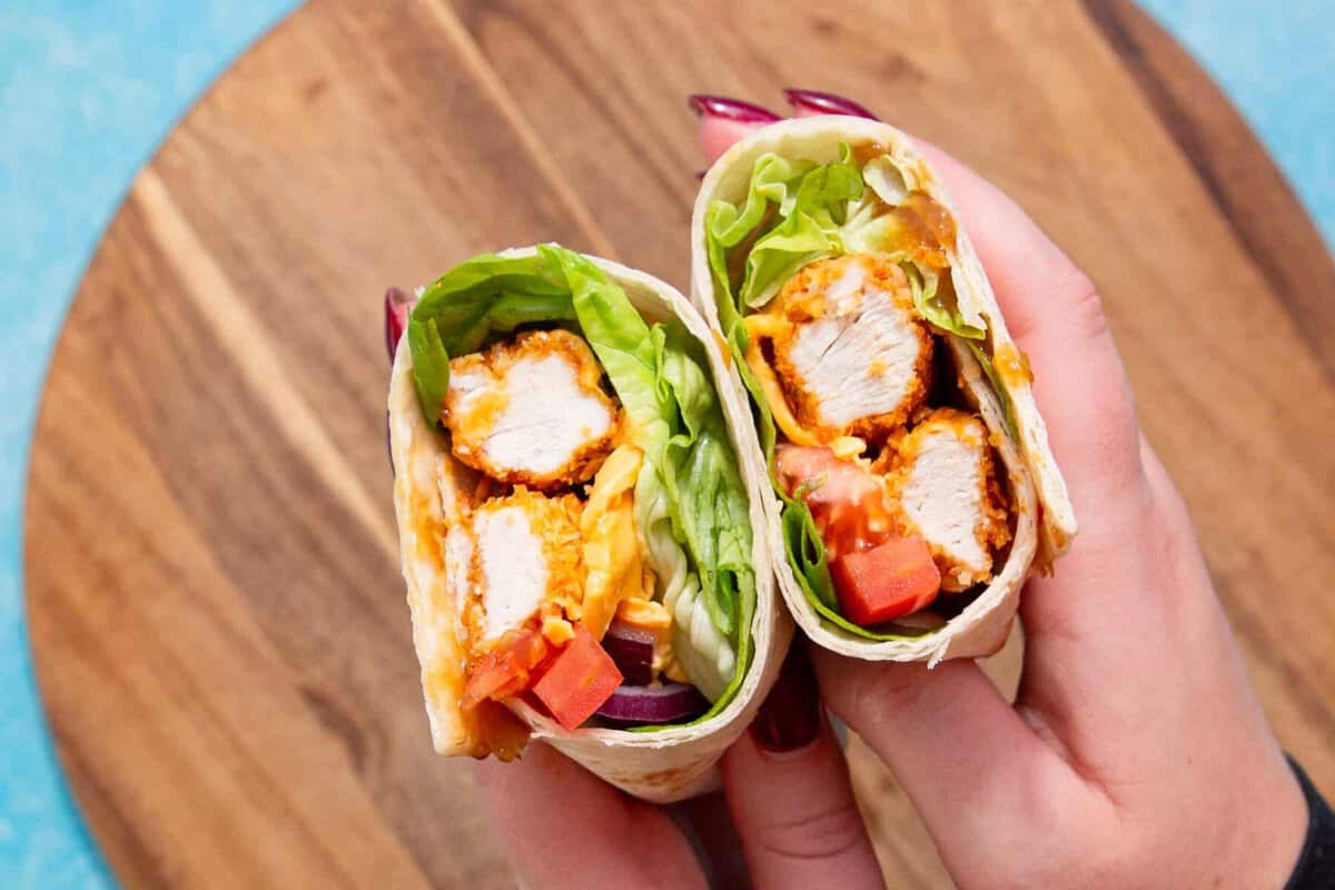 2 hands holding 2 chicken wraps filled with salad.