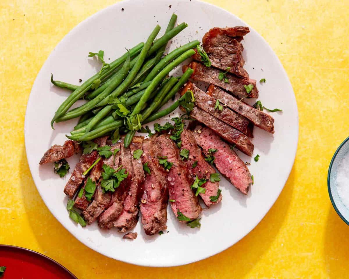 frozen steak in air fryer feature image of perfectly cooked steak that has been sliced and fanned around a white plate next to green beans and sprinkled with parsley