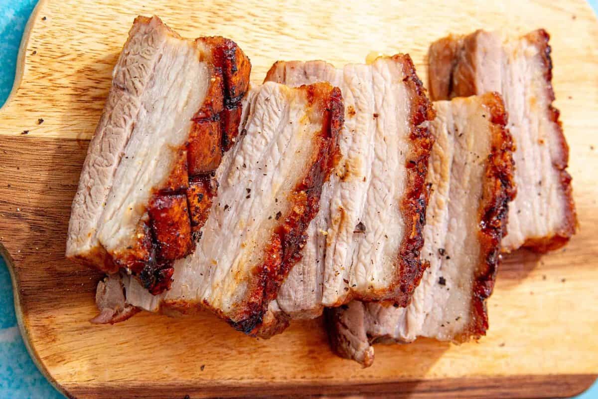 Sliced pieces of crispy, roasted pork belly with golden-brown edges are arranged on a wooden cutting board.