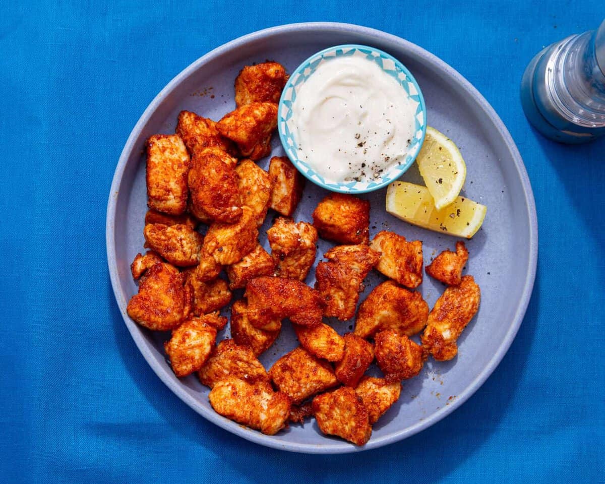 A blue bowl with golden browned and seasoned chicken ieces with wedges of lemon and a little bowl of mayonnaise.