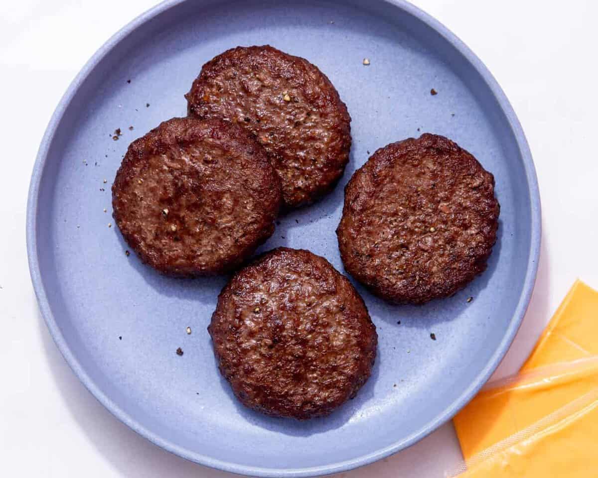 4 cooked, dark browned burgers on a blue plate with some cheese slices in the background.