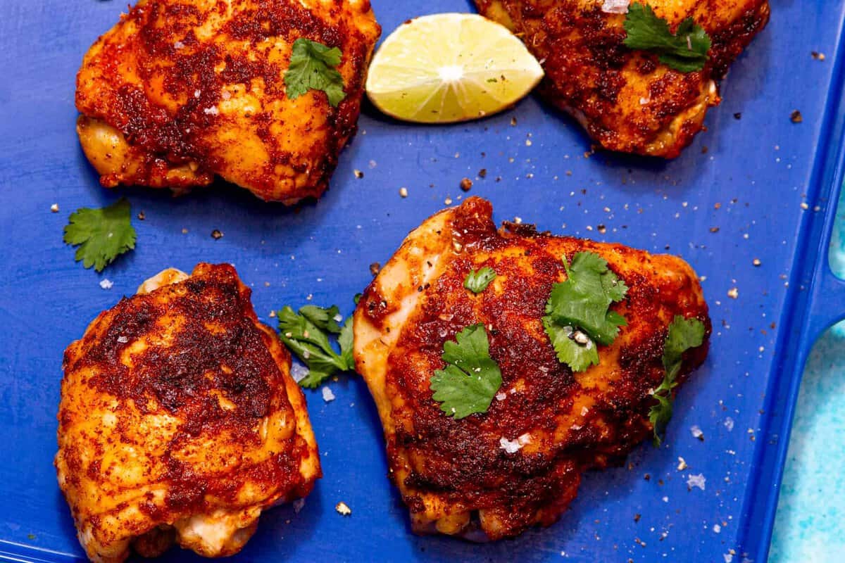 4 golden browned chicken thighs on a blue tray with a lime wedge.