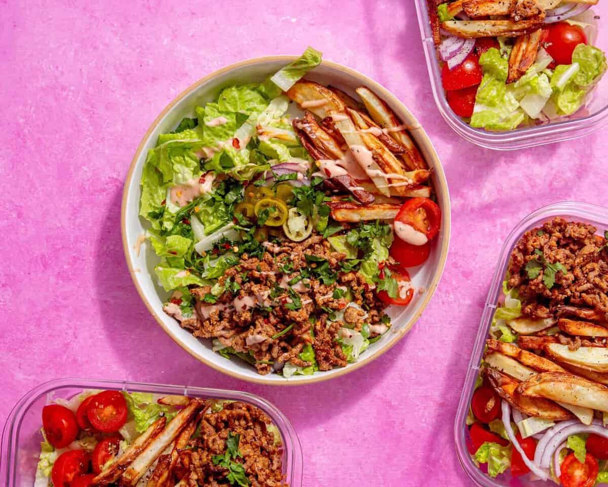 image of prepared burger bowl with other meal prep bowls around it on a pink background