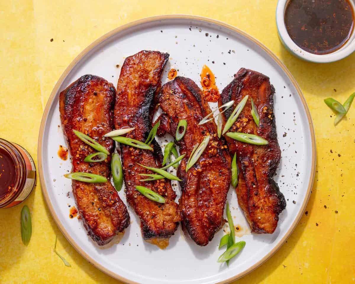 fully air fried pork belly strips on a white plate on a yellow backgorund