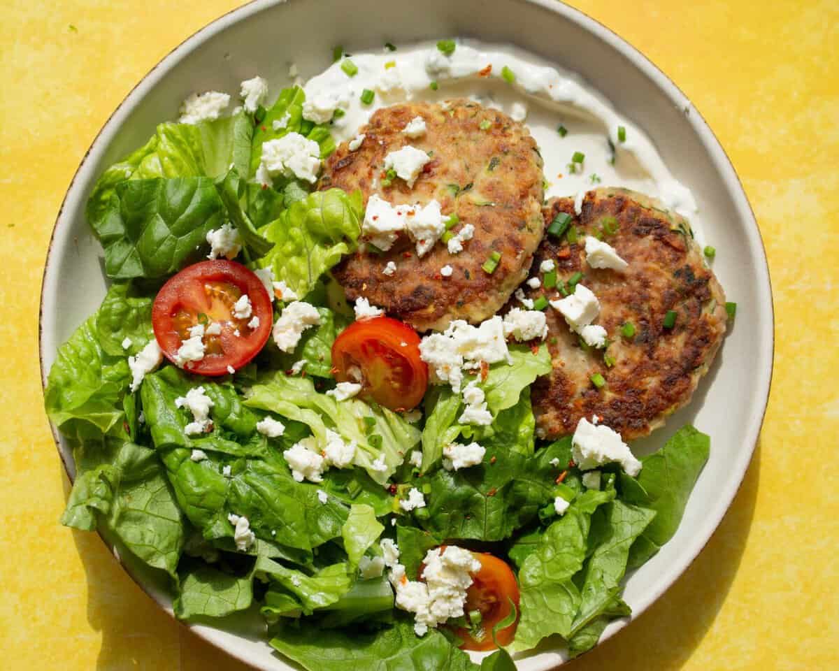 Turkey Burger Salad with lettuce, tomatoes, crumbled feta with a sour cream and chive dip with 2 turkey burgers in a bowl.