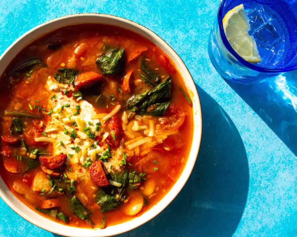 A bowl of chorizo and bean stew with garted cheese and creamy topping.