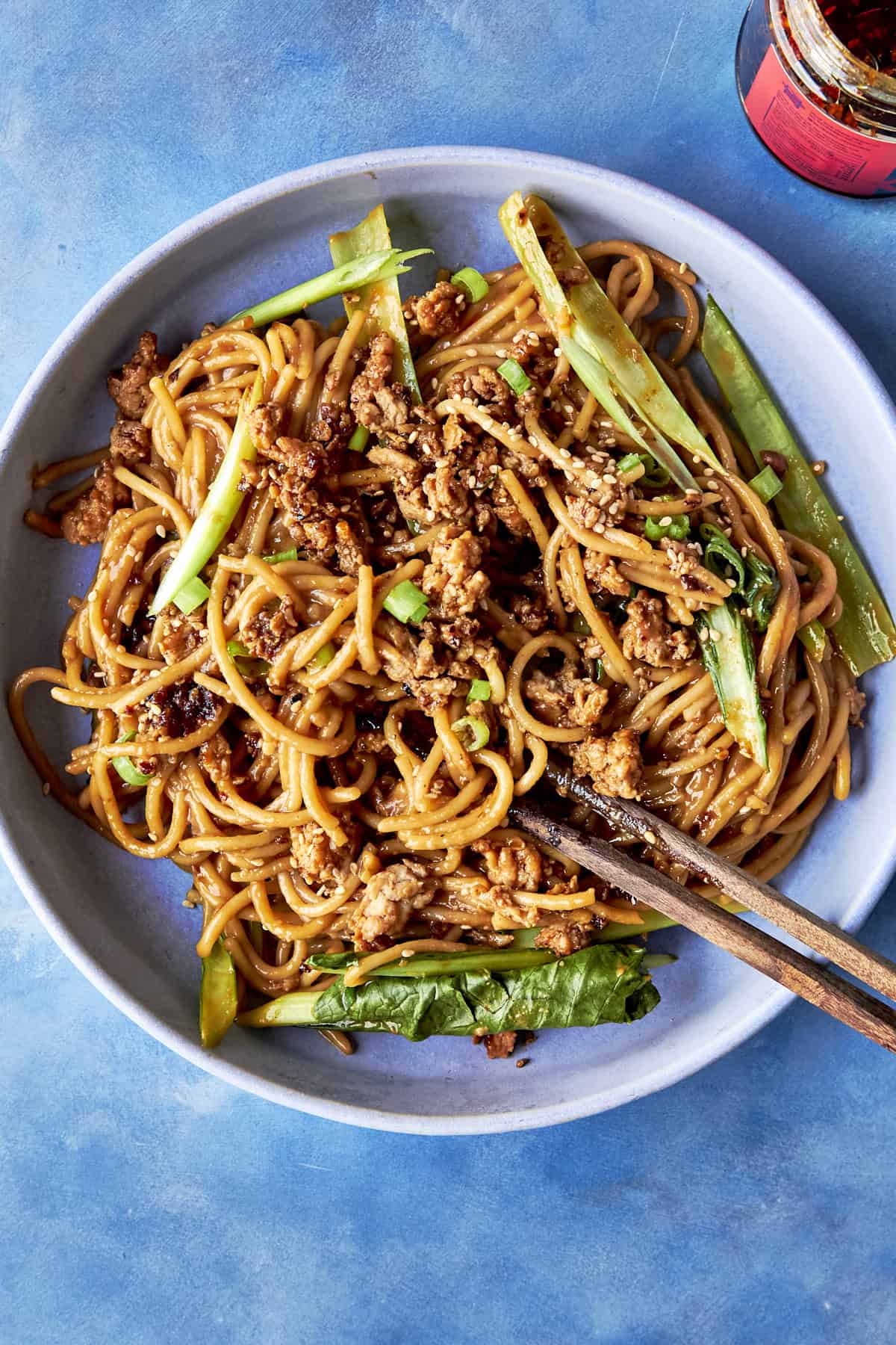 Close-up of dan dan noodles in a bowl with glossy peanut dan dan sauce and crispy chicken mince on top.