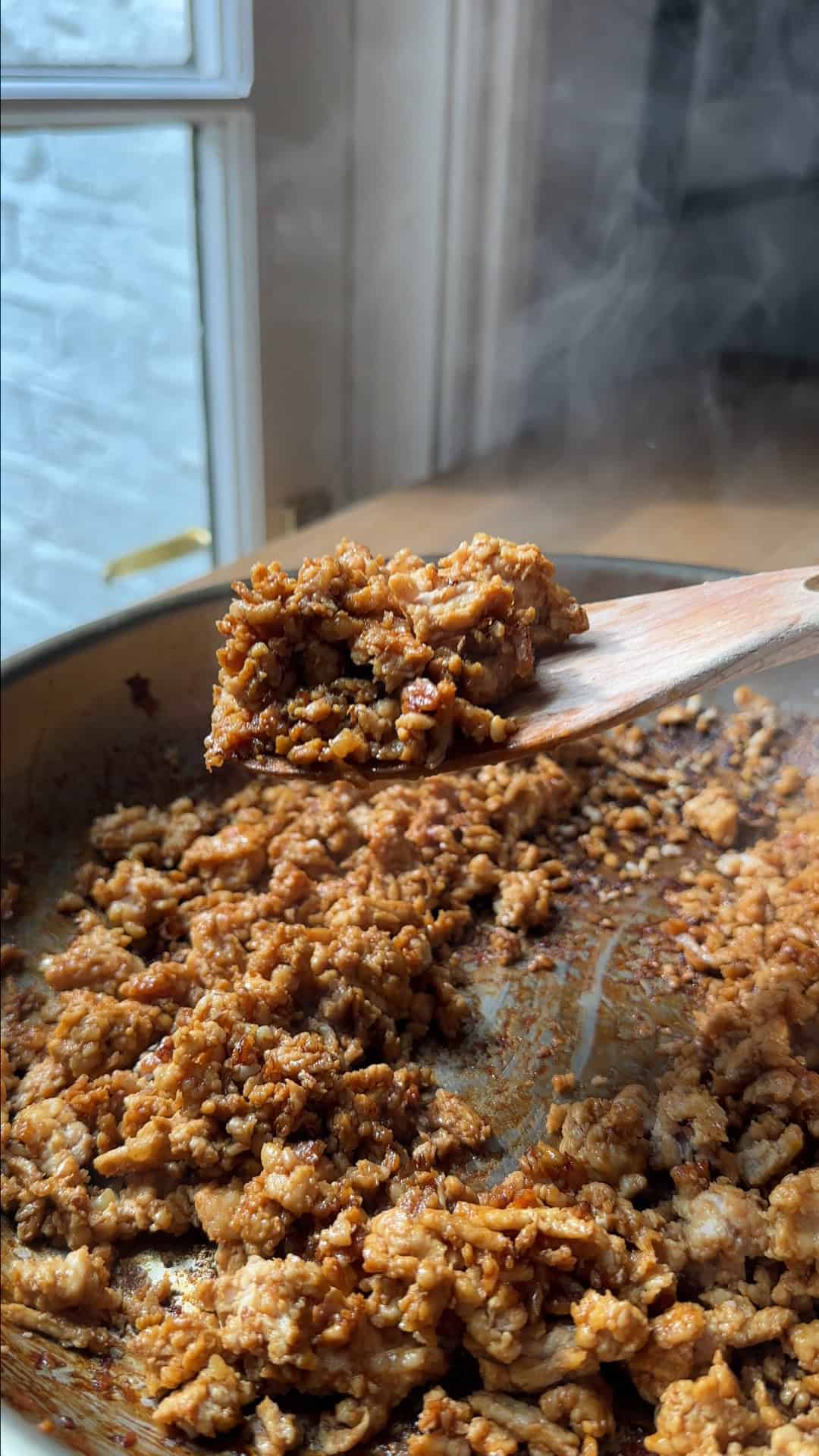 Soy sauce and honey being stirred into crispy browned chicken mince in a pan.