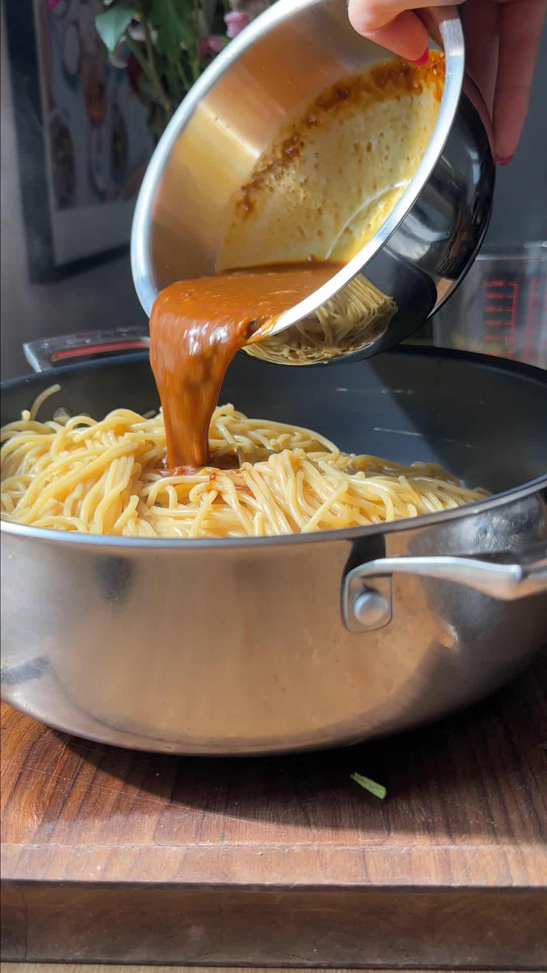 Cooked spaghetti being tossed through the creamy dan dan sauce in a large pan.