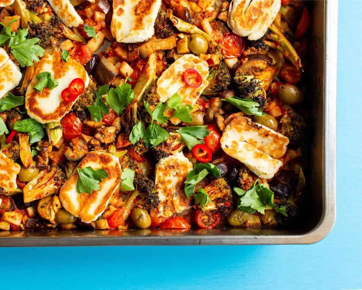 Roasted vegetables in a tray topped with golden browned halloumi and coriander.