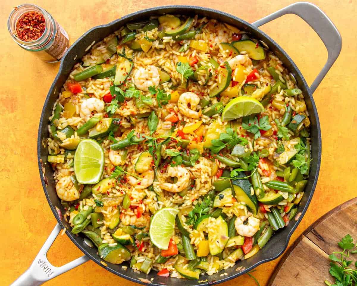 Prawns, rice and vegetables in a large pan topped with lime wedges and parsley.