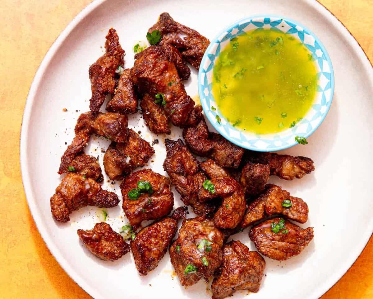 Pieces of browned steak on a plate next to a little bowl of melted butter and herbs.