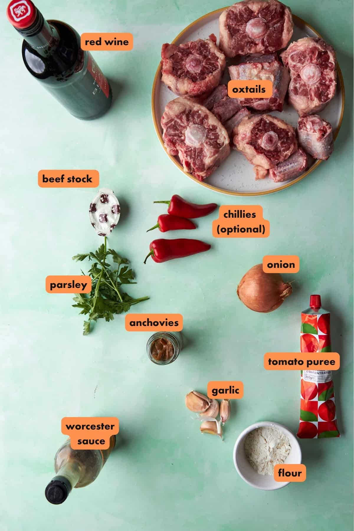Ingredients for braised oxtails laid out flat, including oxtails, red wine, beef stock, garlic and spices.