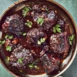 Overhead shot of braised oxtails in a rich glossy sauce, scattered with fresh parsley.