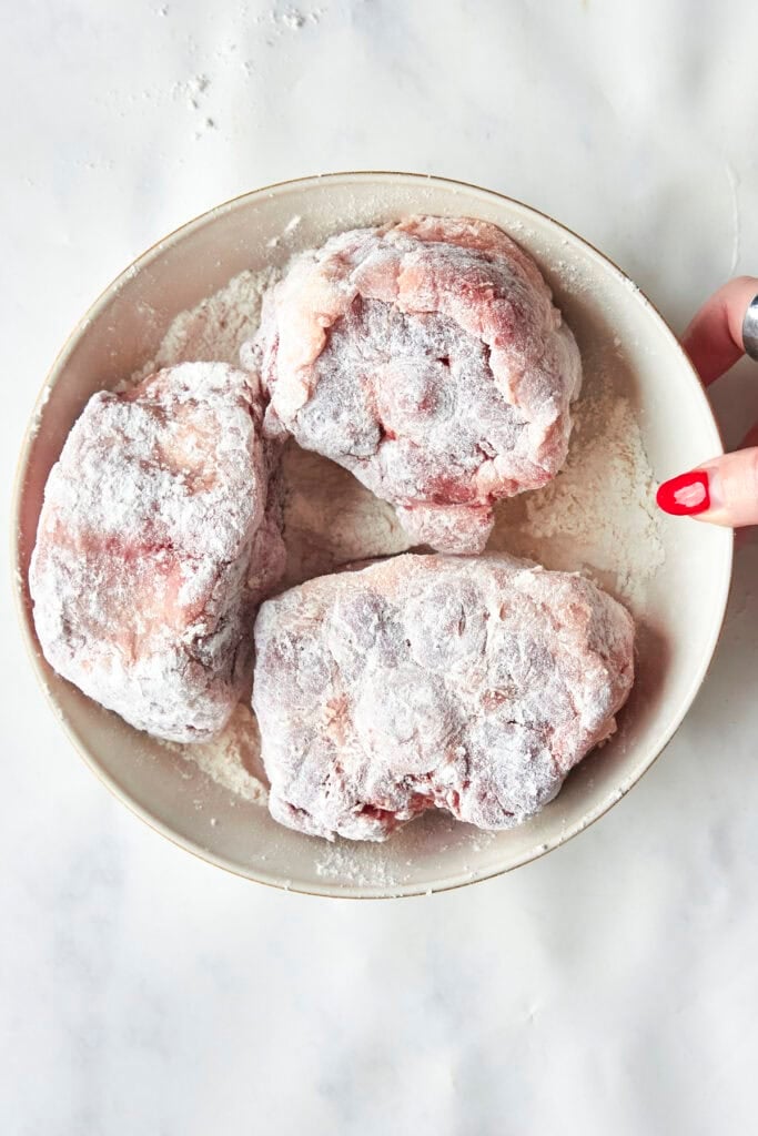 Oxtails being patted dry, seasoned and coated in flour.