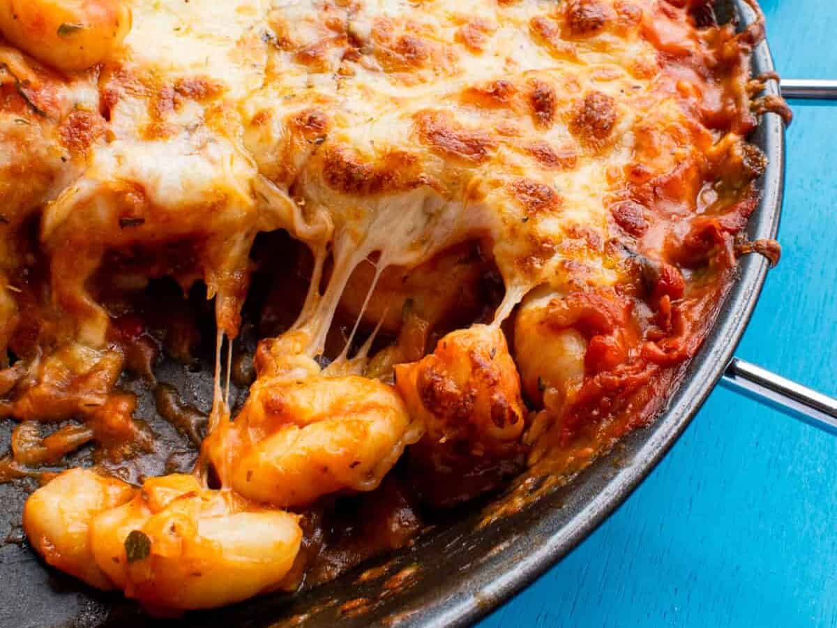Golden browned gnocchi in a large round pan wth a handle with lots of cheese in a pan and a portion removed to show the cheesy middle.