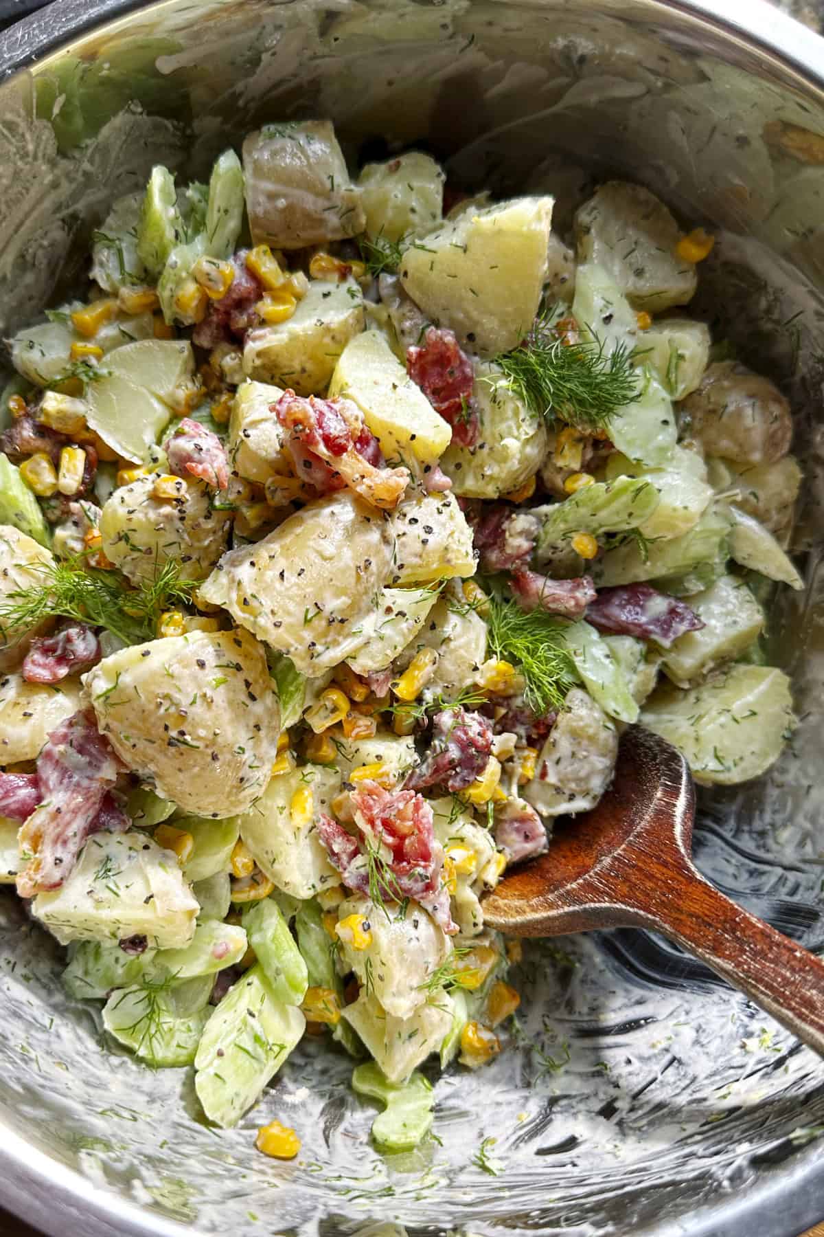 Ingredients for creamy dill potato salad laid out, including new potatoes, cooking bacon, sweetcorn, yoghurt, dill and celery.