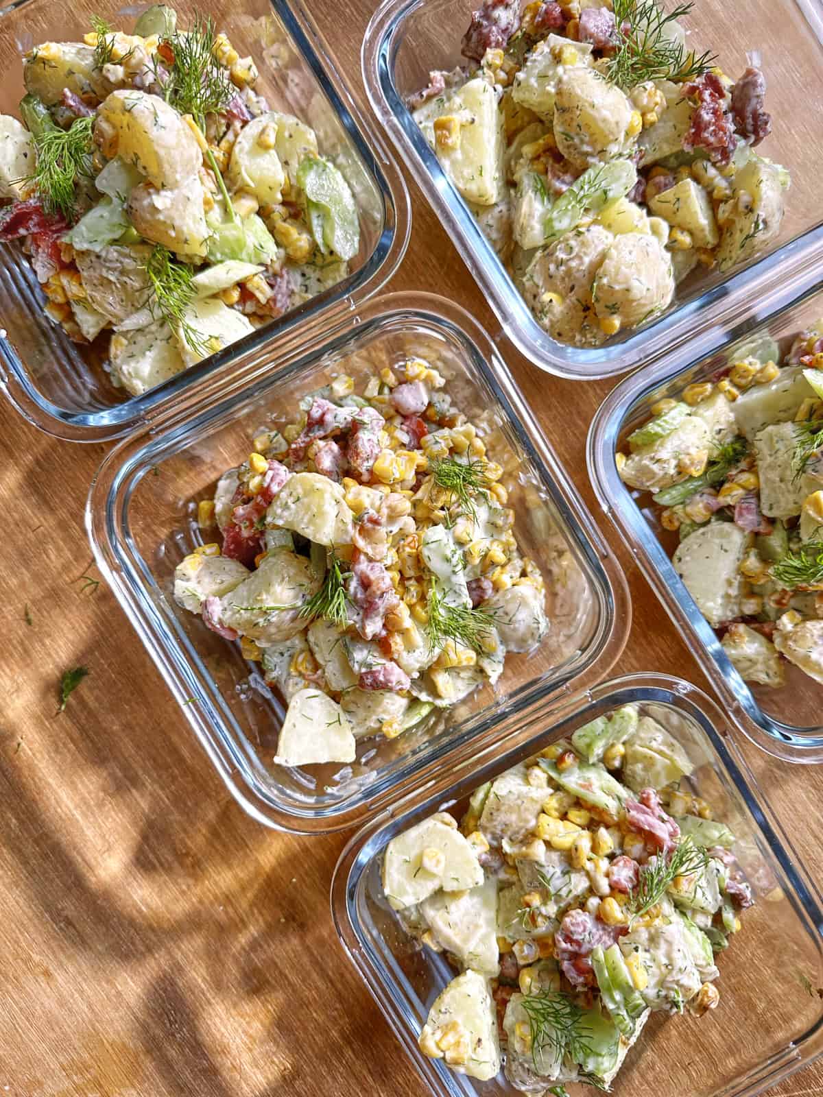 Close-up of creamy dill potato salad in a meal prep container, showing the charred corn, bacon and dill dressing.