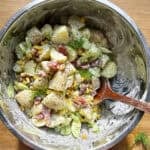 Overhead shot of creamy dill potato salad with crispy bacon and charred sweetcorn, finished with fresh dill.
