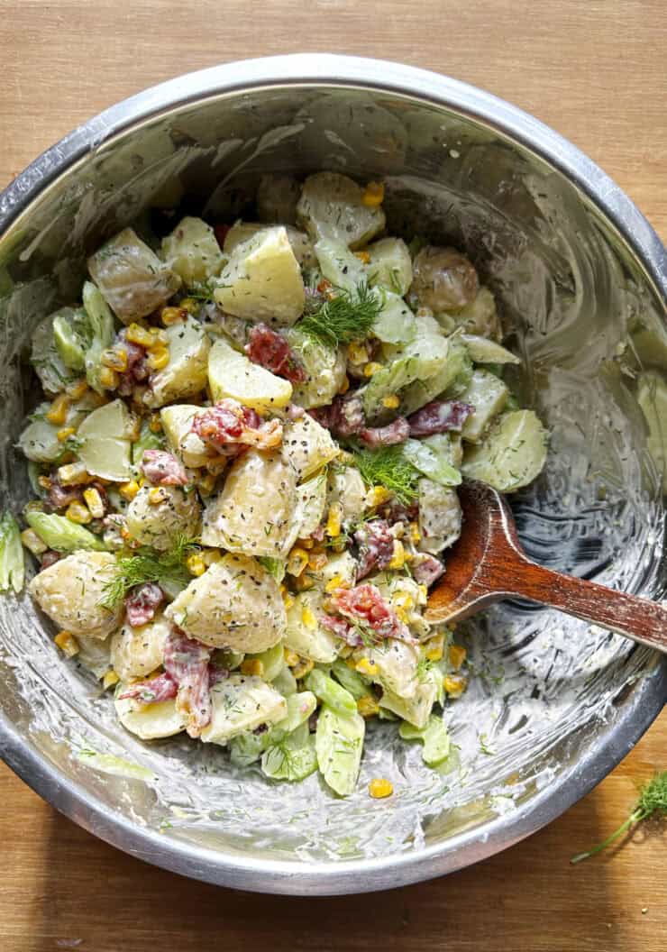 Overhead shot of creamy dill potato salad with crispy bacon and charred sweetcorn, finished with fresh dill.
