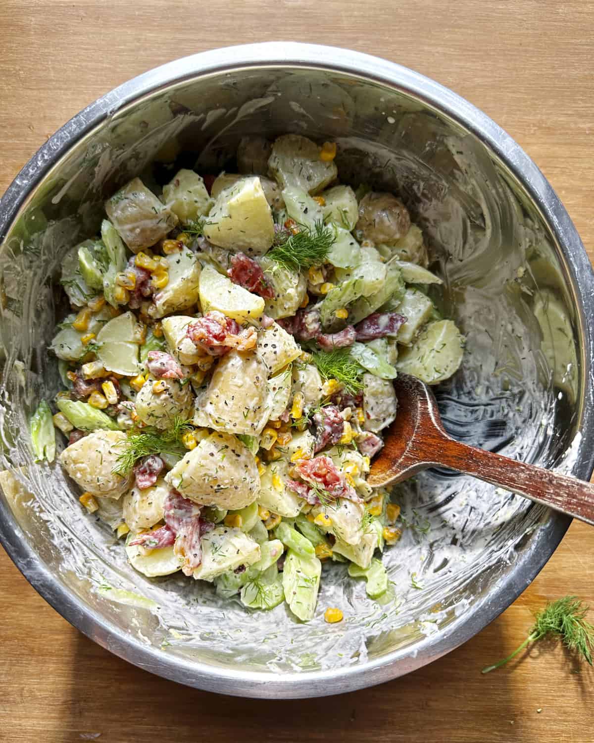 Overhead shot of creamy dill potato salad with crispy bacon and charred sweetcorn, finished with fresh dill.