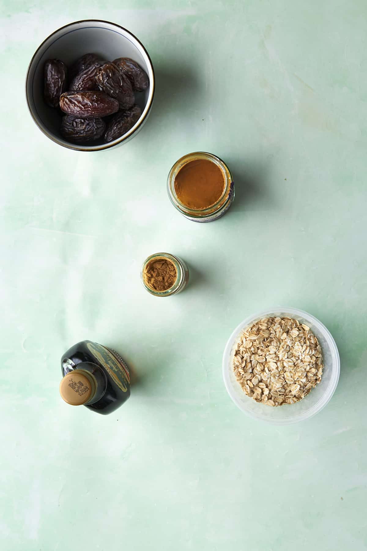 Ingredients for energy balls with dates laid out flat, including medjool dates, almond butter, oats, maple syrup and ground ginger.