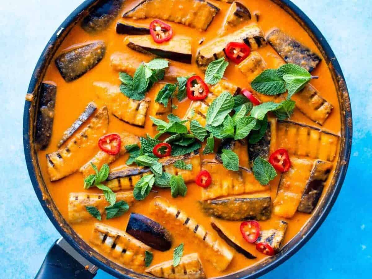 Aubergine curry in a large pan with aubergine charred batons covered in sauce topped with coriander and chillies.