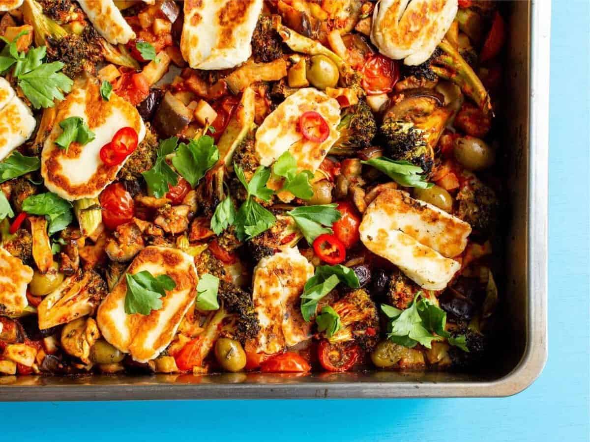 Roasted vegetables in a tray topped with golden browned halloumi and coriander.