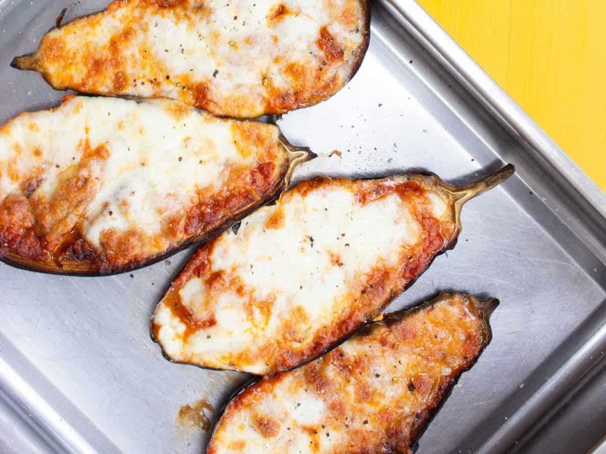 Overhead shot of 4 aubergine halves topped with melted cheese on stainless steel baking tray
