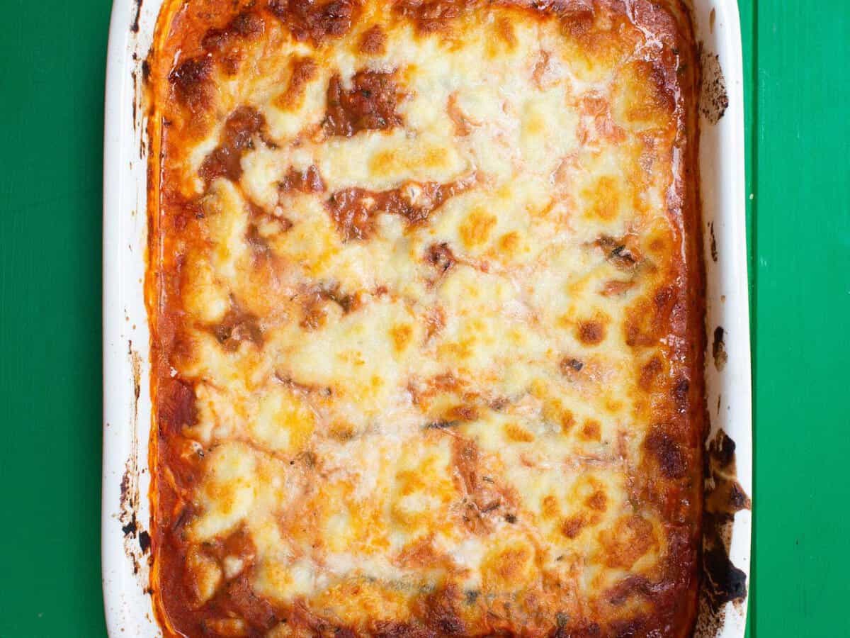 Overhead shot of cooked lasagna in white baking dish on green background