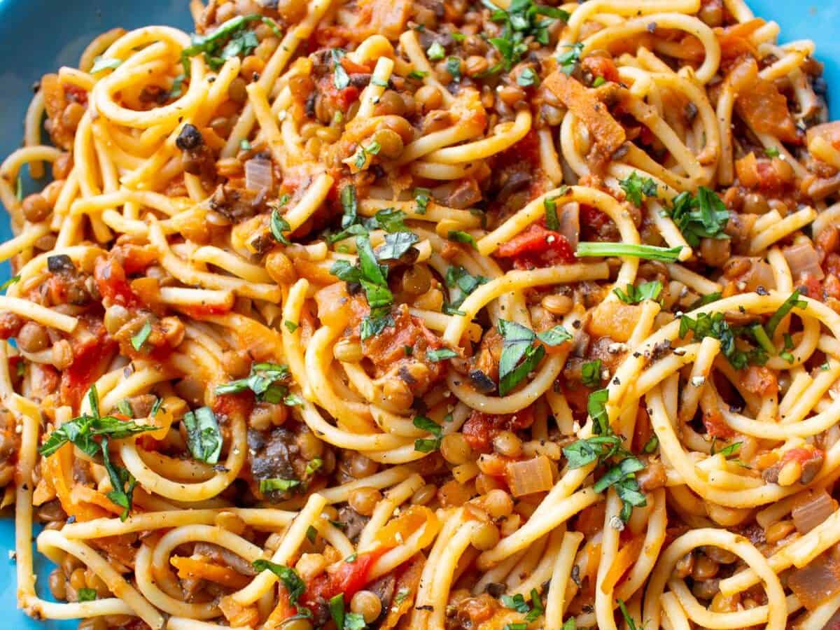Lentil Bolognese served on a blue dish and garnished with chopped basil on an orange background.