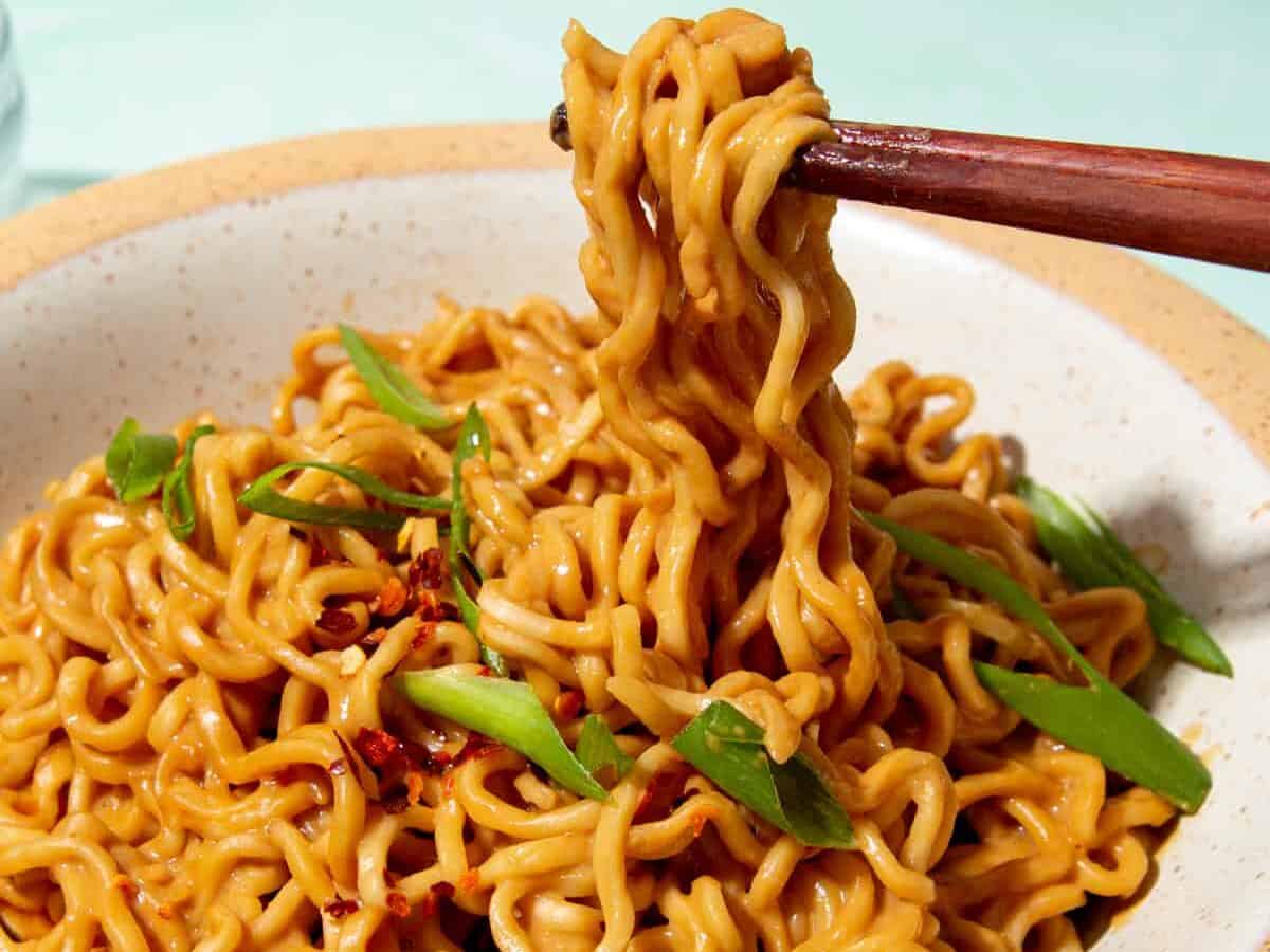 Noodle in a bowl with some noodles held with chop sticks and the dish garnished with sliced spring onion.