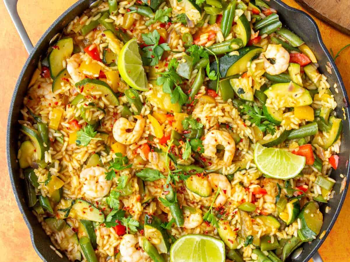 Prawns, rice and vegetables in a large pan topped with lime wedges and parsley.