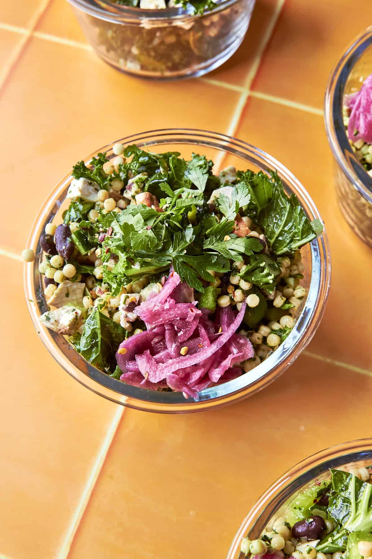Close-up of salsa verde chopped salad in a glass meal prep container topped with parsley and pickled red onion.