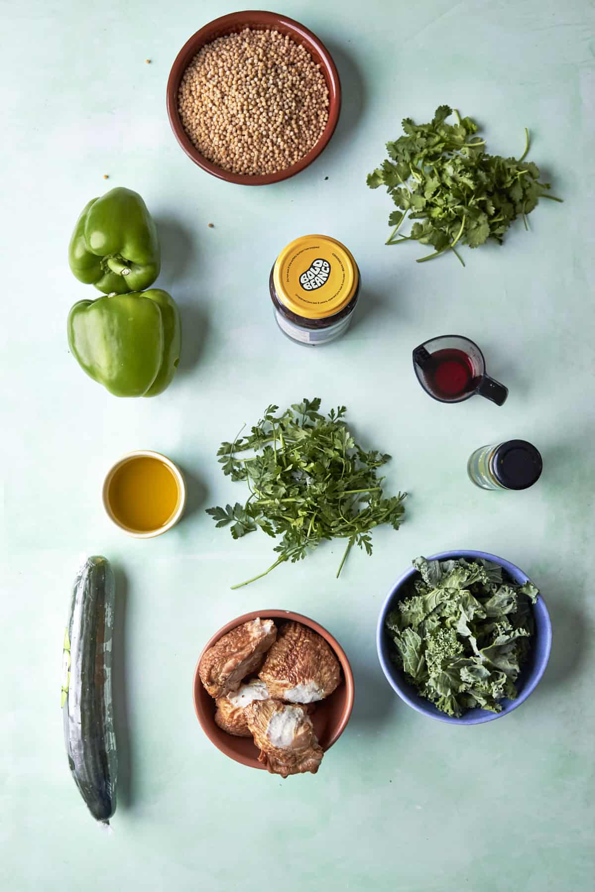 Ingredients for salsa verde chopped salad laid out flat, including kale, giant couscous, chicken, parsley, coriander and capers.